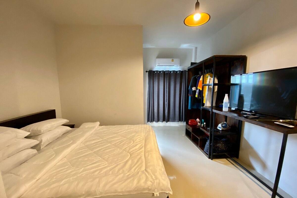 A hotel room with a bed, a TV, a wardrobe, and a hanging light fixture.