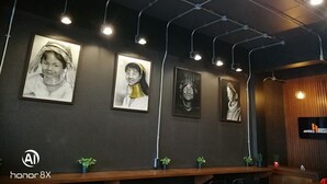 A room with a dark wall, three framed portraits, a wooden reception desk, and a television screen displaying 'JAIDEE HOUSE'. - Jaidee Cafe & Hostel Chiangrai (Chiang Rai)