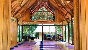 Een ruime houten hal met een hoge plafond en grote ramen, met yogamatten in rijen opgesteld.