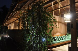 A wooden structure with a green cushioned seating area and hanging lights.