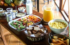 A breakfast buffet with various dishes including fruits, scrambled eggs, and bread.