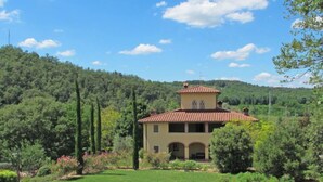 A villa with a red-tiled roof, surrounded by lush greenery and hills.