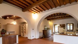 A spacious kitchen with a central island, wooden beams on the ceiling, and a tiled floor.
