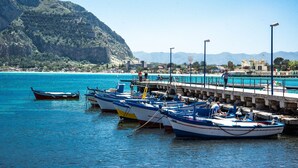 A coastal marina with several boats docked, a pier extending into the water, and a mountainous backdrop. - La Casa di Sara a Mondello by Wonderful Italy (Palermo)