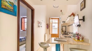 A modern kitchen with a central island, a dining area with a chair, and a hallway leading to a bedroom. - La Casa di Sara a Mondello by Wonderful Italy (Palermo)