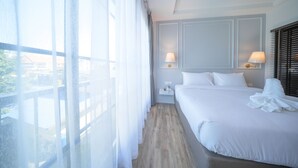 Ein Hotelzimmer mit einem großen Bett, zwei Nachttischlampen, einem Nachttisch und Blick durch transparente Vorhänge.