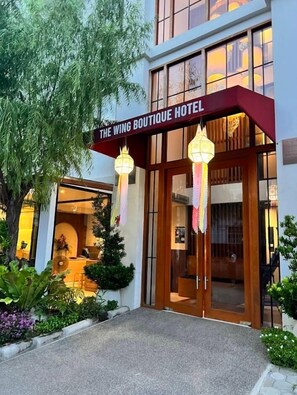 The Wing Boutique -hotellin sisäänkäynti, jossa on kyltti, puiset ovet ja roikkuvat lyhdyt.