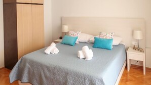 Una cama bien hecha con colcha azul, dos toallas blancas y almohadas estampadas.