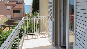 Un balcón con barandilla de metal, puerta corredera de vidrio y vista al mar y otros edificios.