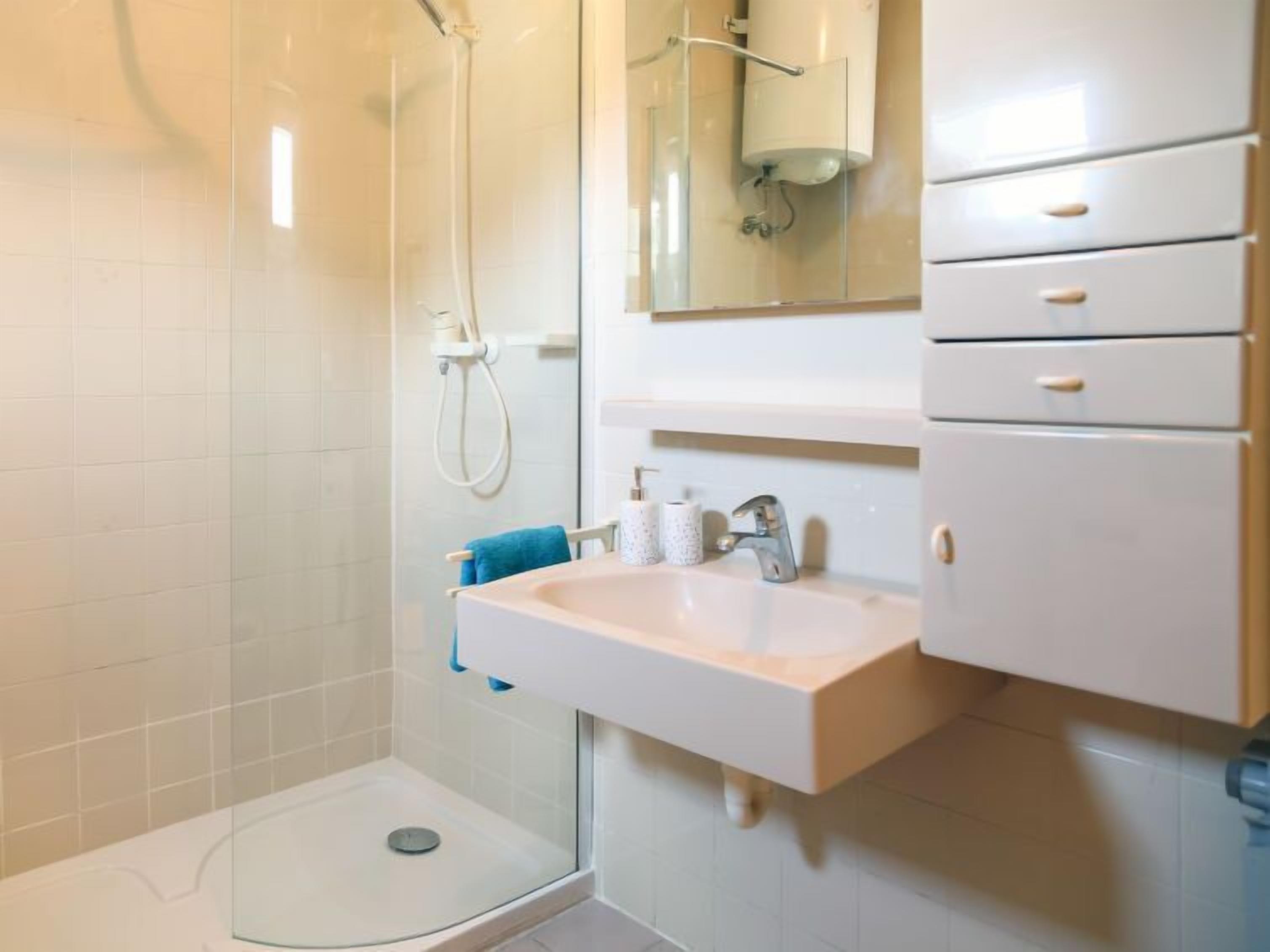 A modern bathroom with a glass shower enclosure, a white sink with a mirror above, and a white cabinet with drawers.