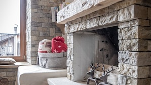 A cozy room with a stone fireplace, a wooden bench, and a rustic barrel. - Casa Ladinia (San Vito di Cadore)