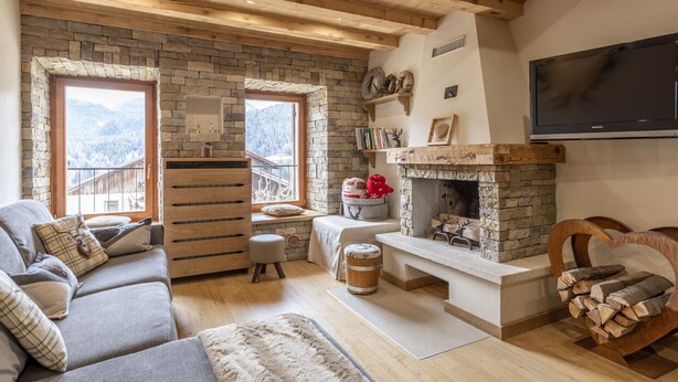 A cozy living room with a stone fireplace, wooden beams, and a large window overlooking a snowy mountain. - Casa Ladinia (San Vito di Cadore)