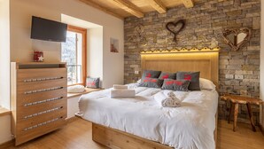 A bedroom with a stone wall, a wooden bed, a TV, and a wooden dresser. - Casa Ladinia (San Vito di Cadore)