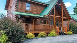 A log cabin with a porch, a chimney, and a green roof.