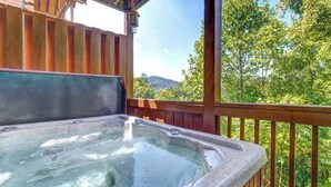A hot tub on a wooden deck with a view of trees and hills.