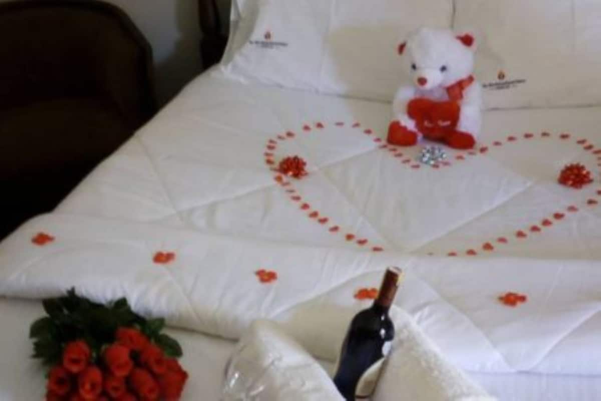Cama com edredom branco com desenho de coração e rosas vermelhas.