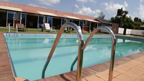 A swimming pool with metal ladders, a covered area with chairs, and a building with large windows and a red roof.