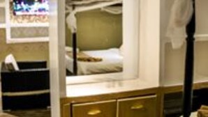 A compact hotel room with a bunk bed, a small desk, and a TV mounted on the wall.