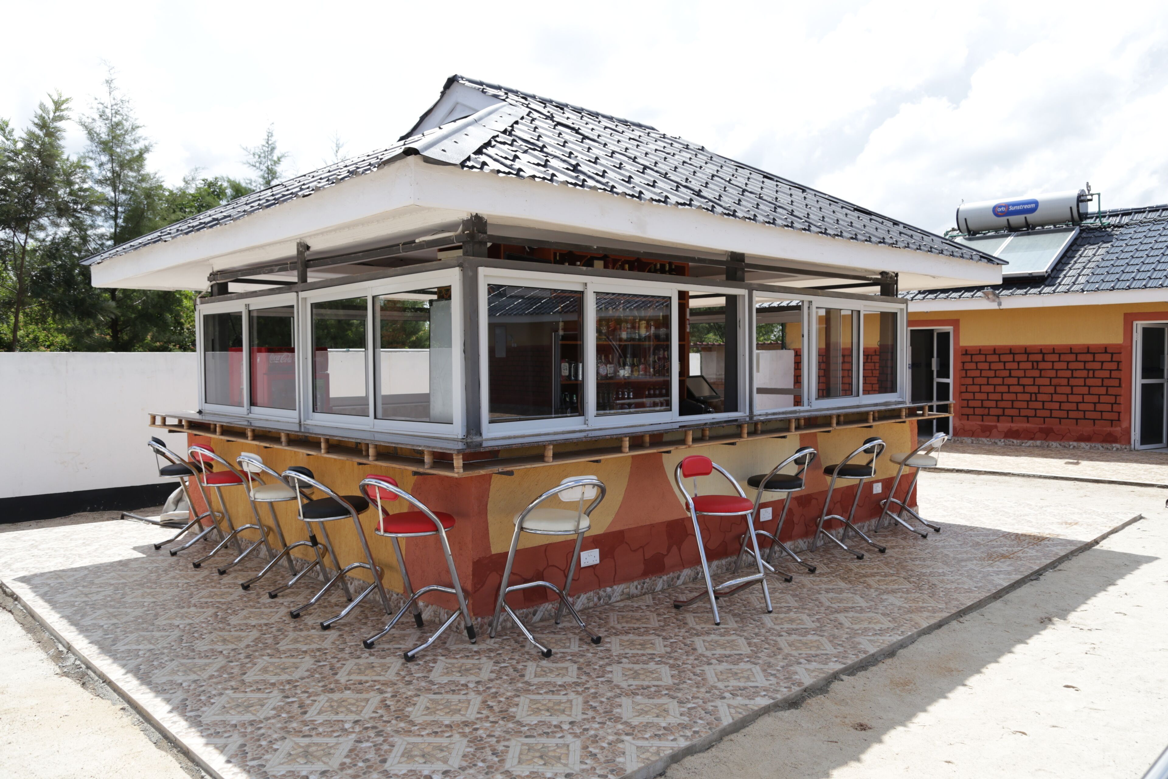 En hyggelig udendørs café med et tagtækket tag, overdækket siddeområde og række af metalstole.