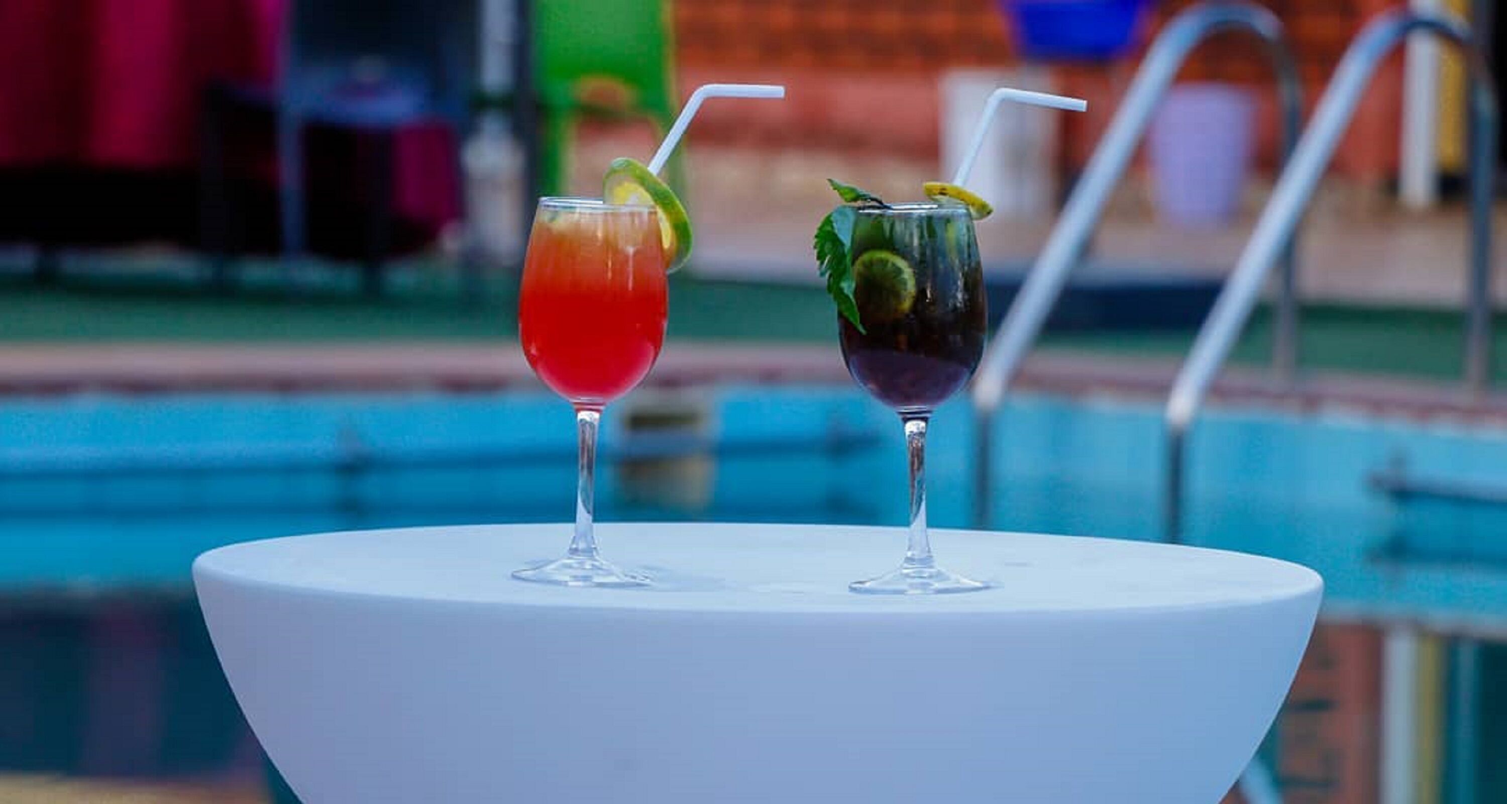Two cocktails on a white table by a poolside.