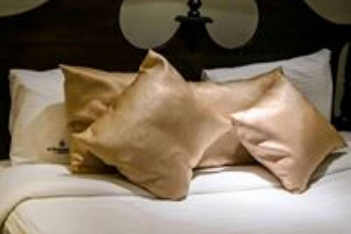 Uma cama com cabeceira escura e várias almofadas.