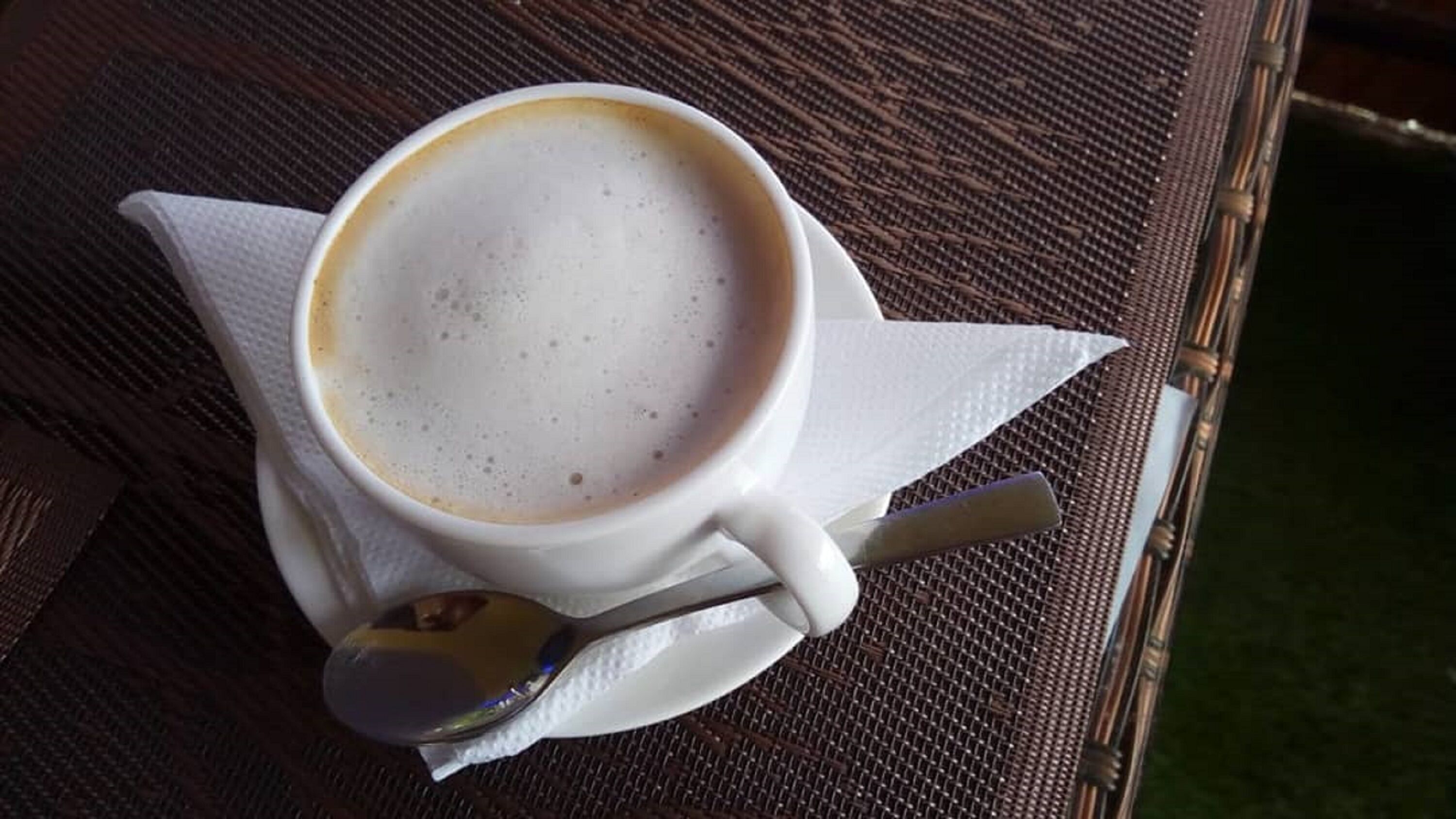 En kop kaffe på et vævet bord med en ske og en serviet.