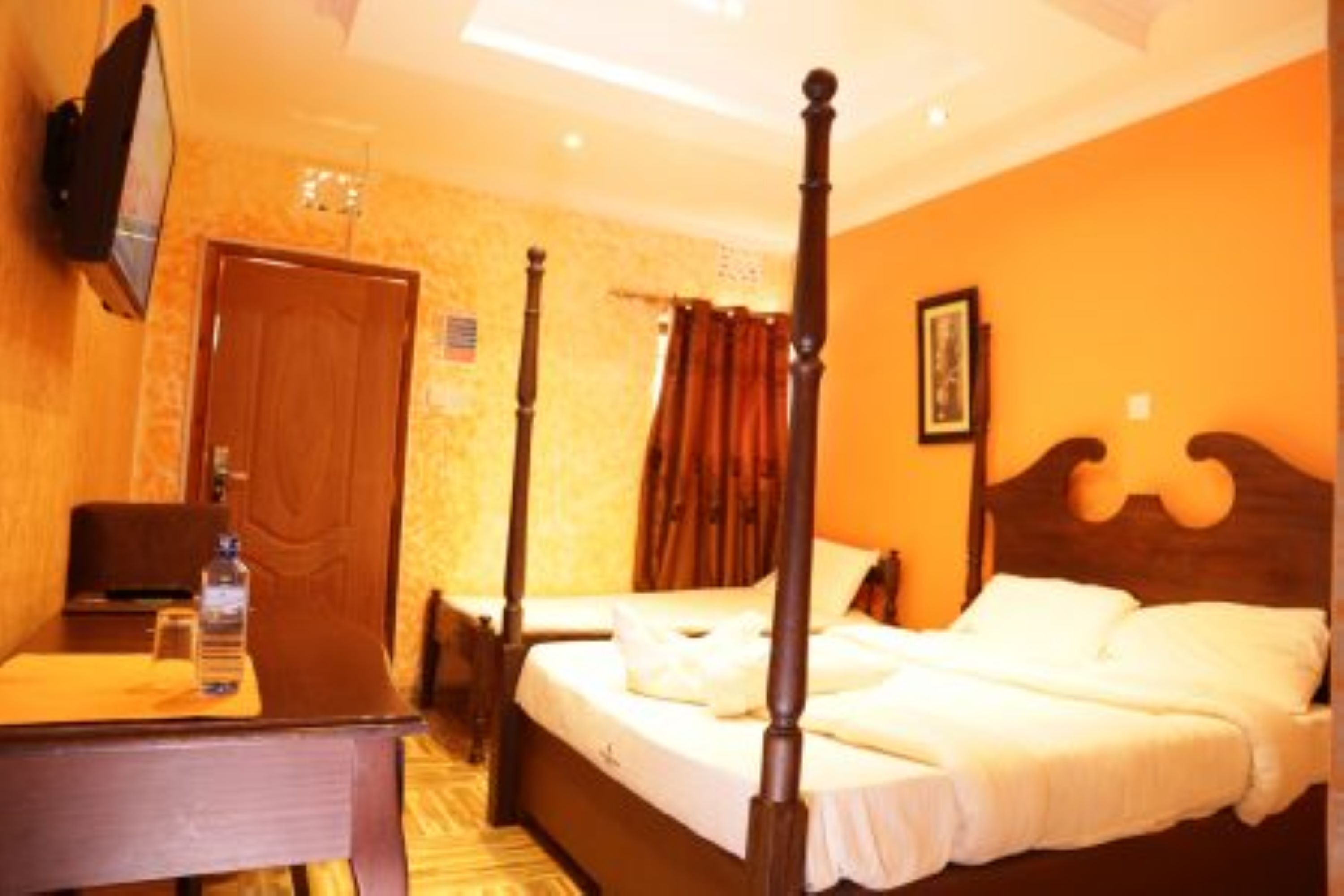 A four-poster bed in a hotel room with a wooden desk and a television on the wall.