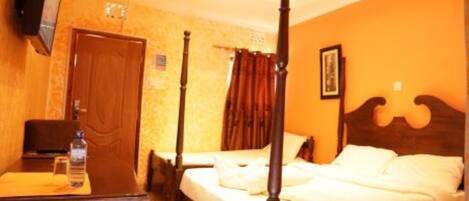 A four-poster bed in a hotel room with a wooden desk and a television on the wall.