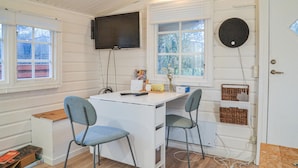 A compact room with a white desk, two grey chairs, a mounted TV, and a door with a basket on the right.
