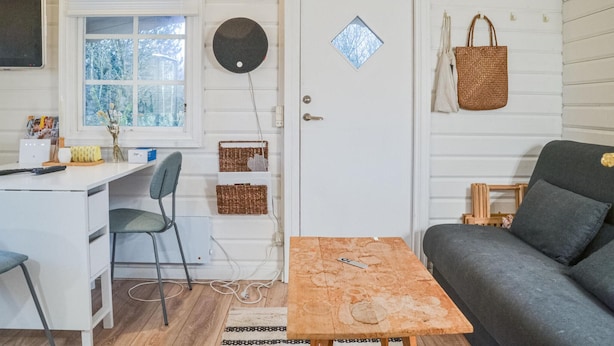 A cozy room with a desk, a chair, a sofa, a small table, and a door with a window.