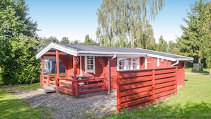 A red wooden cabin with a porch, a small table, and a bench.