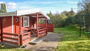 A red wooden cabin with a porch, a table, and a bench.