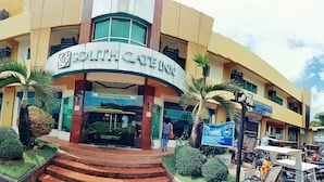 A South Gate Inn hotel with a modern facade, a glass entrance, and a parking area with cars and motorcycles.