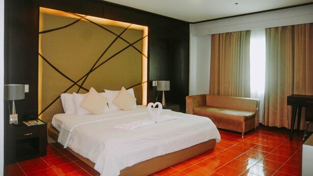 A hotel room with a large bed, a sofa, a desk, and a lamp.