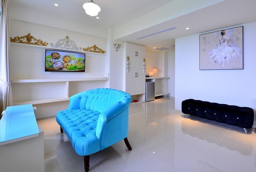 A modern living room with a blue armchair, a black sofa, a flat-screen TV, and a painting on the wall.