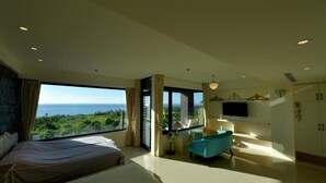 A modern hotel room with a large bed, a seating area with a blue chair, a TV mounted on the wall, and a view of the ocean. - Sunlight Gallery landscape B&B (Chenggong)