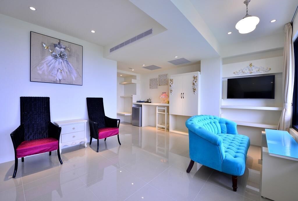 Una sala de estar moderna con un televisor de pantalla plana, un sillón azul y dos sillas con cojines rojos.
