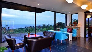 A modern interior with a large window overlooking a scenic view, a seating area with a blue sofa and a wooden cabinet. - Sunlight Gallery landscape B&B (Chenggong)