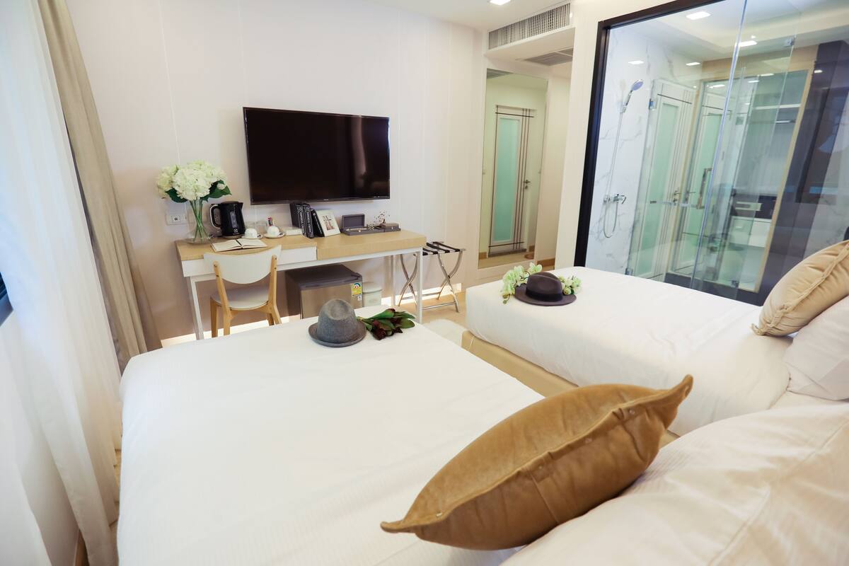 Une chambre d’hôtel avec un lit, un bureau avec une télévision, une machine à café et une fenêtre donnant sur une salle de bain.