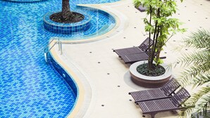 Ein Swimmingpool mit blauen Fliesen, umgeben von Liegestühlen und Topfpflanzen.