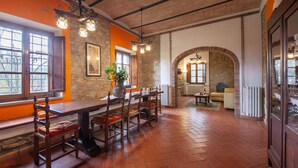 Un espace repas avec une longue table en bois et des chaises, des murs en pierre et un sol en briques.