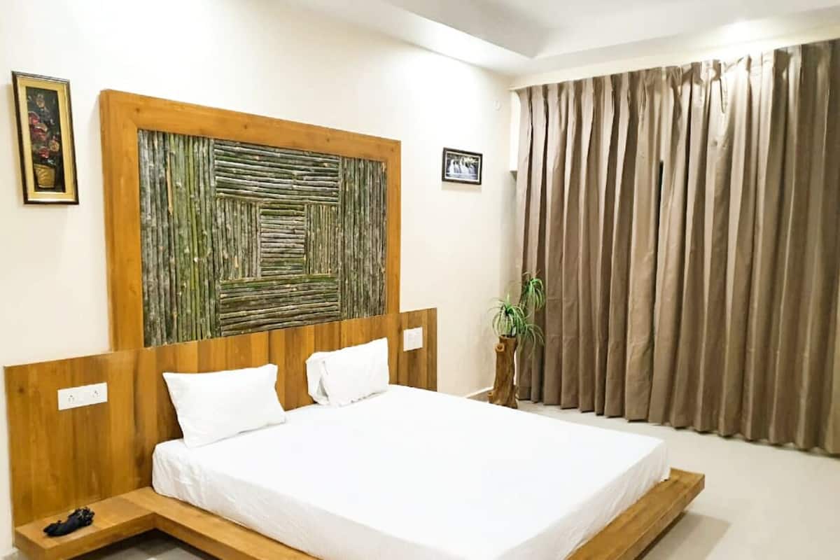 Une chambre d’hôtel moderne avec un cadre de lit en bois, du linge de lit blanc, une grande œuvre d’art abstraite accrochée au mur, une plante en pot et une vue sur la ville à travers les rideaux.
