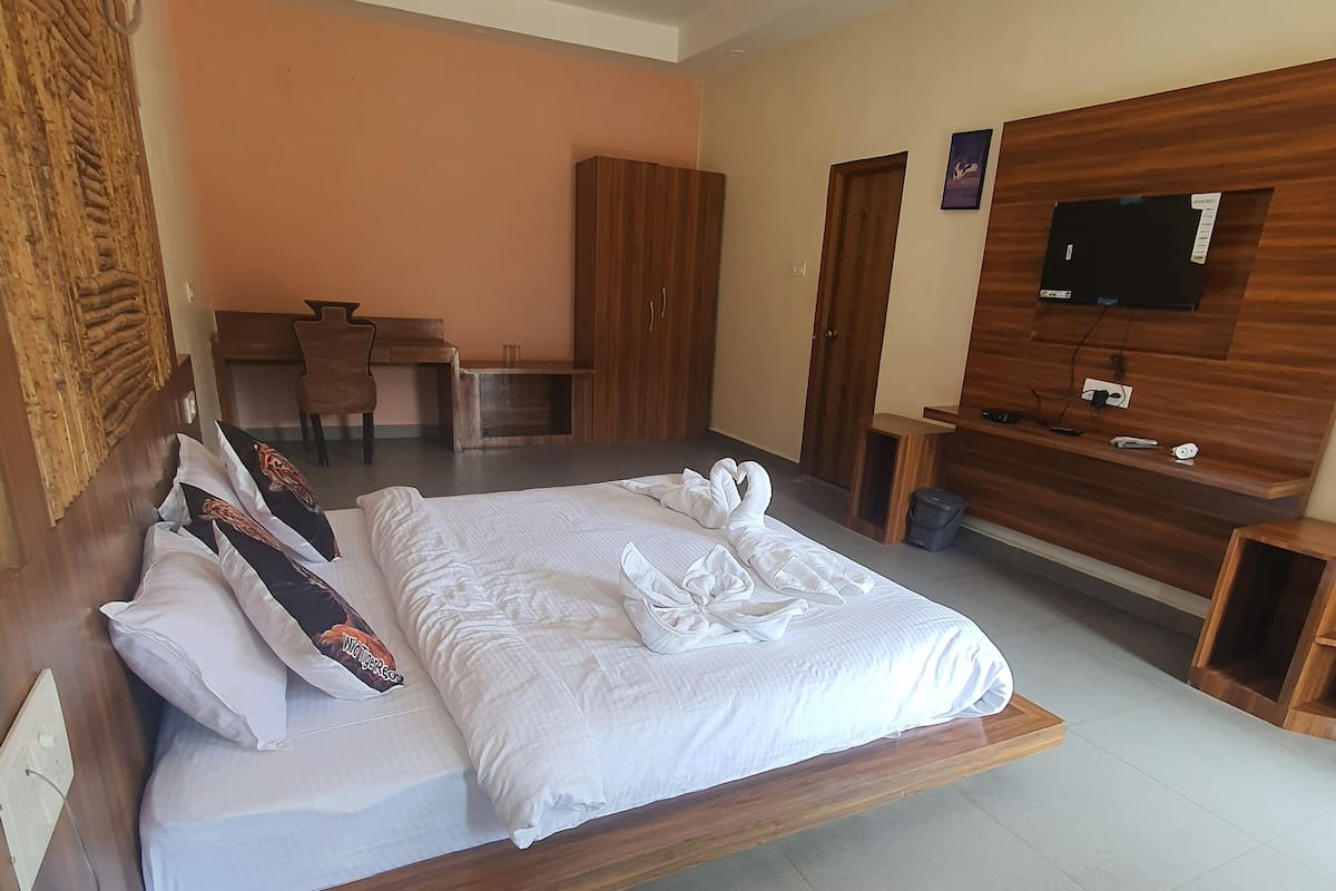 Une chambre d’hôtel avec un grand lit, une tête de lit en bois, un bureau avec une chaise, une armoire et un téléviseur posé sur un meuble en bois.