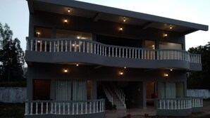 A modern two-story house with a balcony on each floor, a staircase leading to the upper level, and a paved driveway.