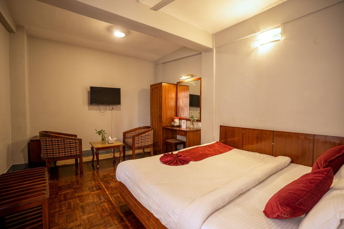 Een hotelkamer met een houten bed, een bureau, een stoel en een aan de muur bevestigde televisie.