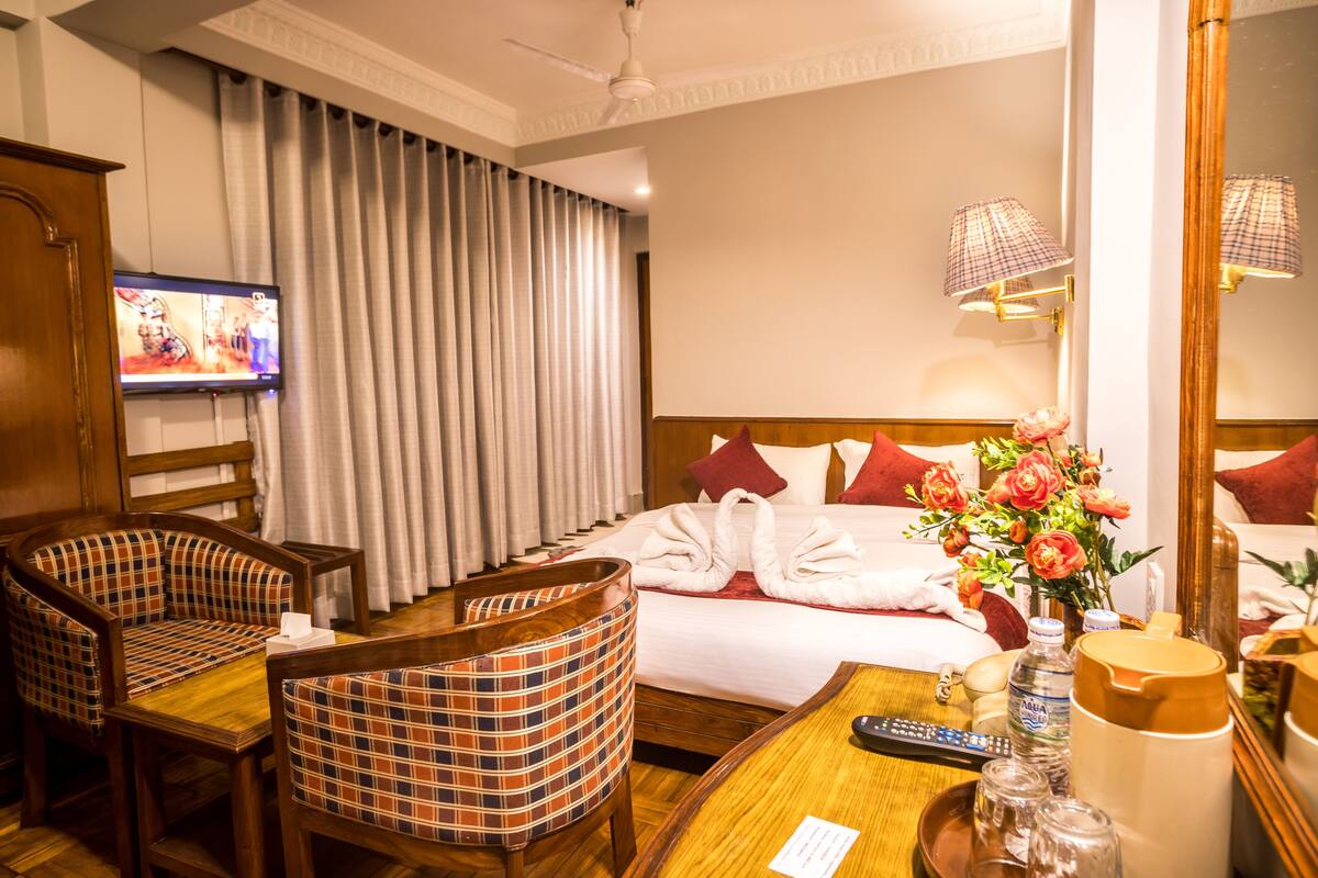 Een hotelkamer met een bed, een televisie, een bureau met een afstandsbediening, een stoel en een spiegel.