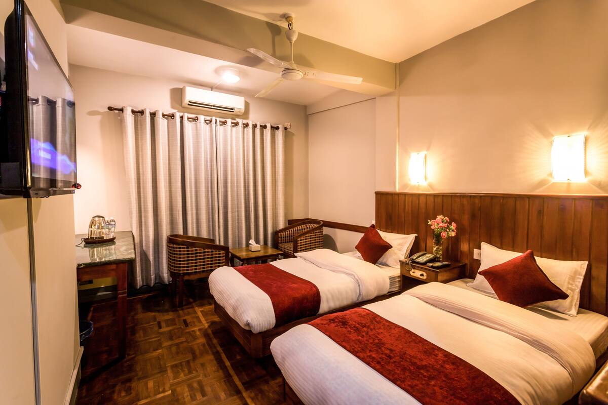 Een hotelkamer met twee bedden, een bureau, een stoel, een airconditioner en een plafondventilator.