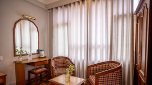 Quarto com escrivaninha de madeira, duas cadeiras xadrez, um espelho e janela com cortinas.