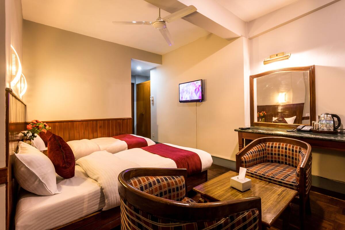 Een hotelkamer met twee bedden, een televisie, een spiegel, een tafel met zakdoosjes en een plafondventilator.