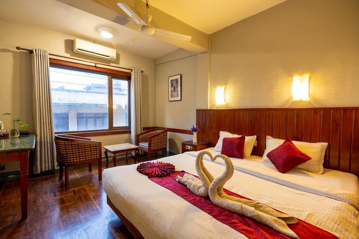 Hotelkamer met een bed, twee nachtkastjes, een stoel, een bureau, een airconditioner, een raam met gordijnen en een wandlamp.